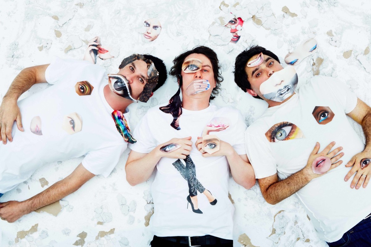 Three people wearing white shirts are lying down with paper cutouts of eyes, lips, hands, and legs on top of them.
