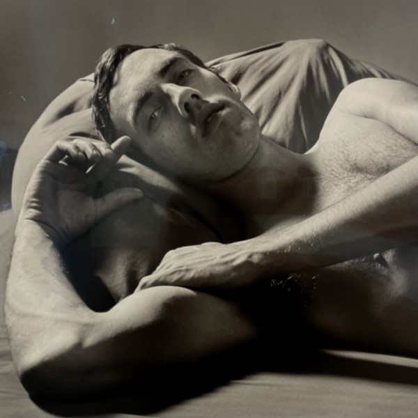 A black-and-white photo of a shirtless man, lying down and resting his head on a beanbag.