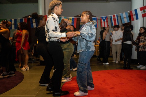 A man and woman dance in a ballroom among a group of people dancing in pairs.