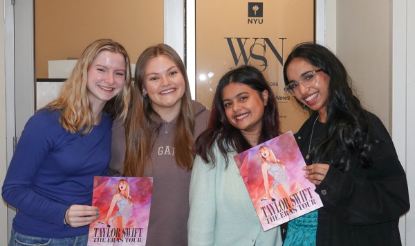 Emily Genova, Natalie Thomas, Naisha Roy and Manasa Gudavalli stand in front of a door posing with "The Eras Tour" posters.