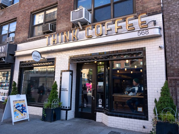 A white brick storefront with a lit up sign across the top reading “Think Coffee.”