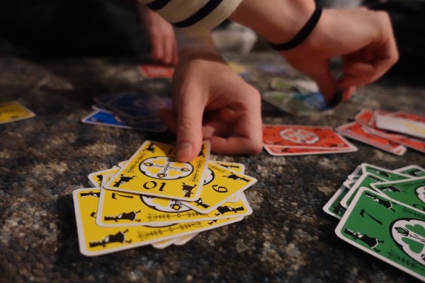 A close up of people playing a card game. There are two hands putting down cards. There are red, yellow, green, and blue cards.
