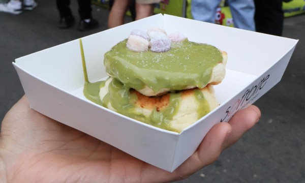 Two Japanese cheesecakes with a green syrup and marshmallows on them in a white square container.