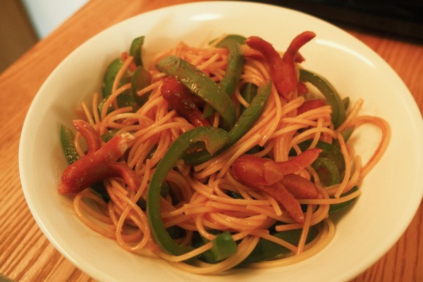 A plate with spaghetti, sausages, and green peppers.