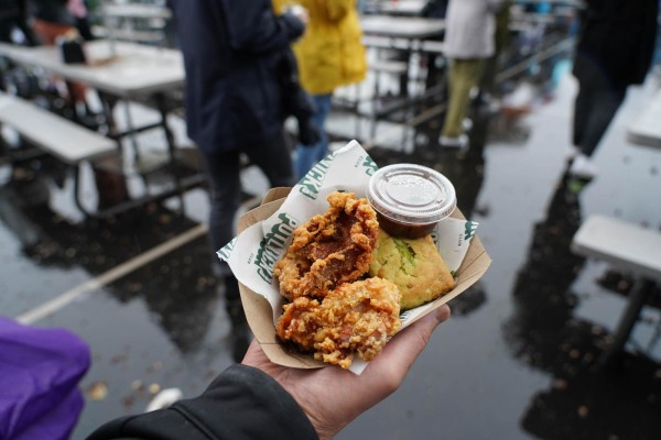 A hand is holding a cardboard plate that has fried chicken, sauce and a pastry in it.