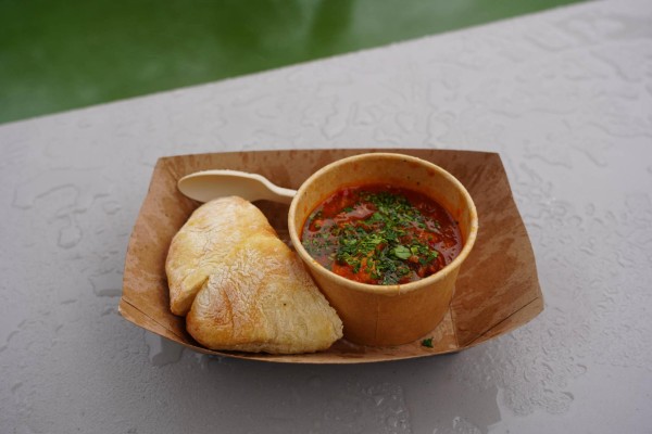 A cardboard plate with bread and red soup with green herbal leaves on top.