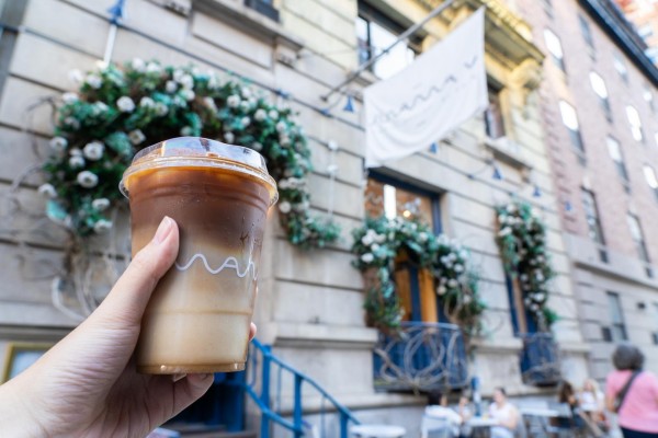 A hand holding a pumpkin pie latte in front of Maman on 67 University Place.