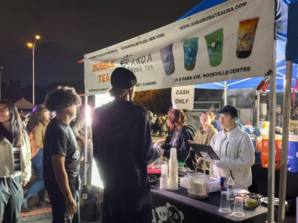 Two people order at an outdoor stand with a sign labeled “ANDA BOBA TEA”.