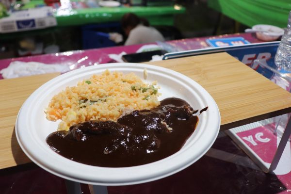 A white paper plate holding fried rice with a dark sauce covered on parts of it.