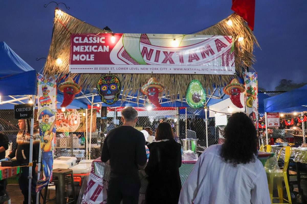 People standing in front of a Mexican-style tent with a sign that says “Classic Mexican Mole” and “Nixtamal”.