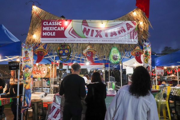 People standing in front of a Mexican-style tent with a sign that says “Classic Mexican Mole” and “Nixtamal”.