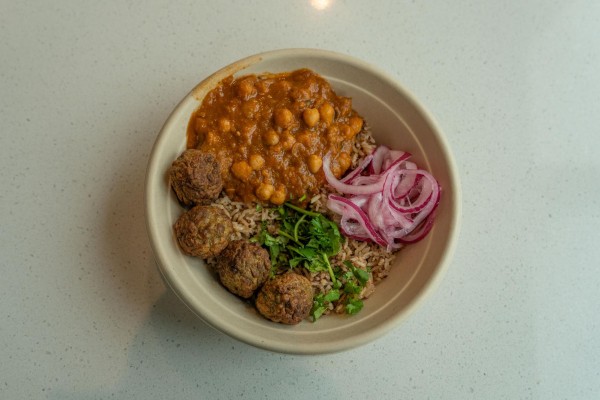 A bowl containing rice, meatballs, cilantro, onions, and a chickpea stew.