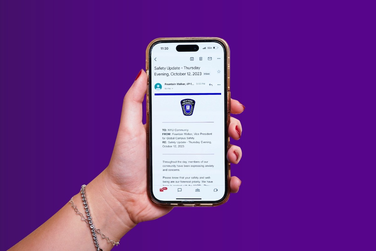 A hand holding a phone displaying N.Y.U. Vice President for Global Campus Safety Fountain Walkers email in front of a purple background.