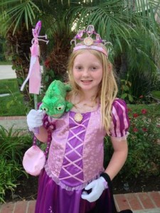 A girl in a purple and pink dress with a crown on her head and a stuffed chameleon on her shoulder, dressed as Rapunzel from the Disney movie “Tangled.”