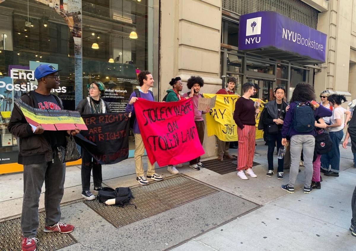 People standing in front of the N.Y.U. Bookstore, holding protest signs and banners.