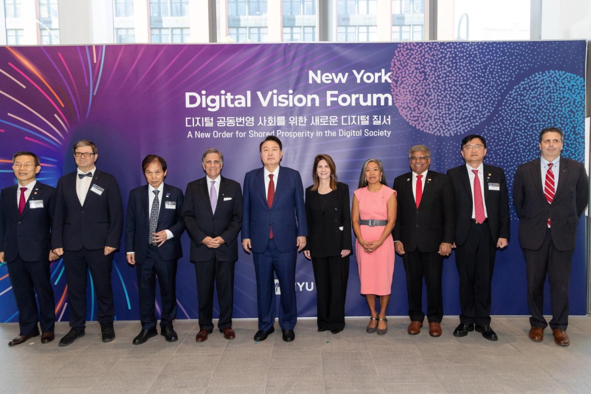 Ten men and women in suits and dresses stand in front of a purple background that says “New York Digital Vision Forum”.
