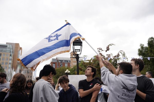 A crowd of men looking up at an Israeli flag being waved in the air in a park.