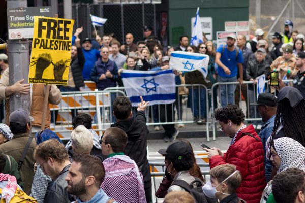 Two crowds of people face one another from behind fences on opposite sides of the street, yelling at each other with flags and signs.