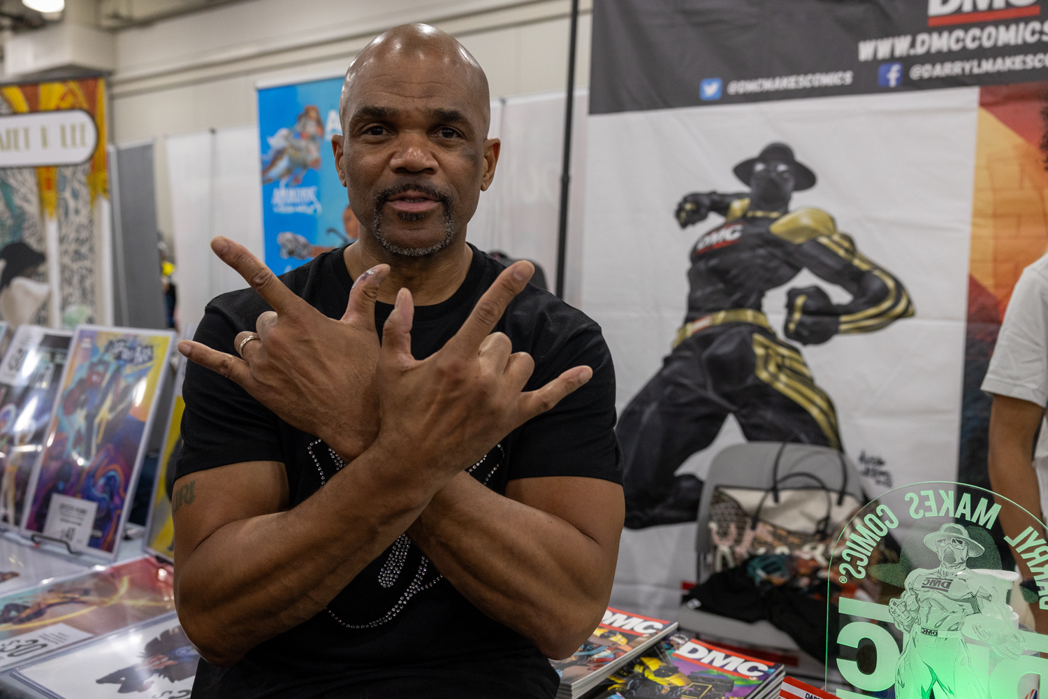 Darryl McDaniels (Run DMC) poses in front of a Run DMC booth filled with posters and merchandise.