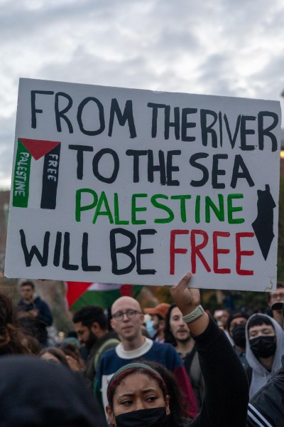 A protestor holds a sign saying “FROM THE RIVER TO THE SEA PALESTINE WILL BE FREE.”