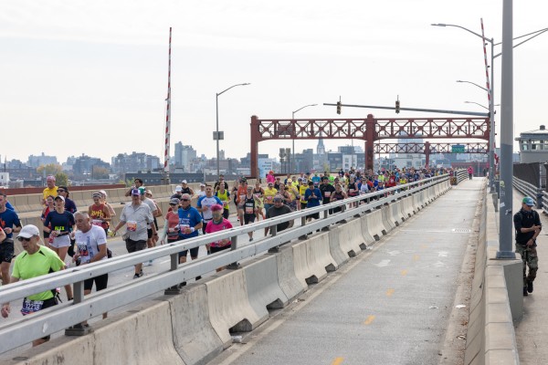 People in various colored outfits run across the Pulaski Bridge into Queens from Brooklyn.