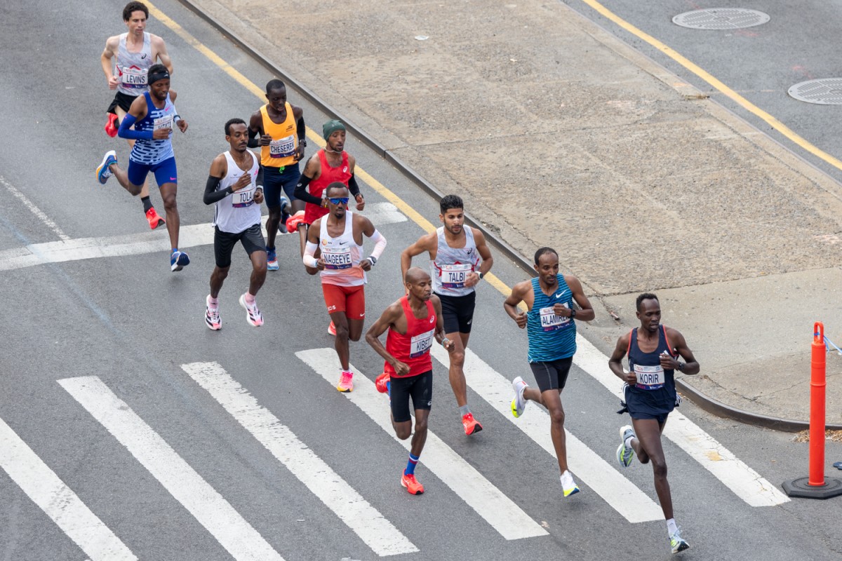 The men's elite field runs in various colored outfits. Fourth to last Tamirat Tola wears a white top and black shorts.