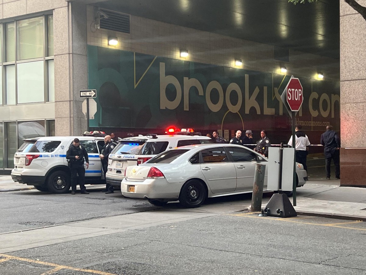 Two police vans and a white car are parked on the street besides a red STOP sign and a red DO NOT ENTER sign. A group of police standing around the vehicles are talking near police tape.