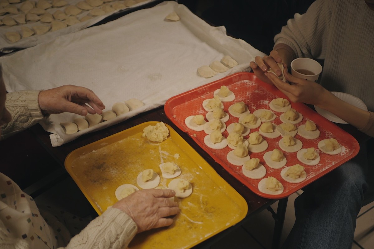 Hands of two female volunteers over pierogi trays.