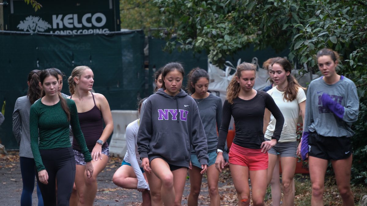 A group of women athletes wearing running outfits standing in a row in a park getting warmed up for a run.