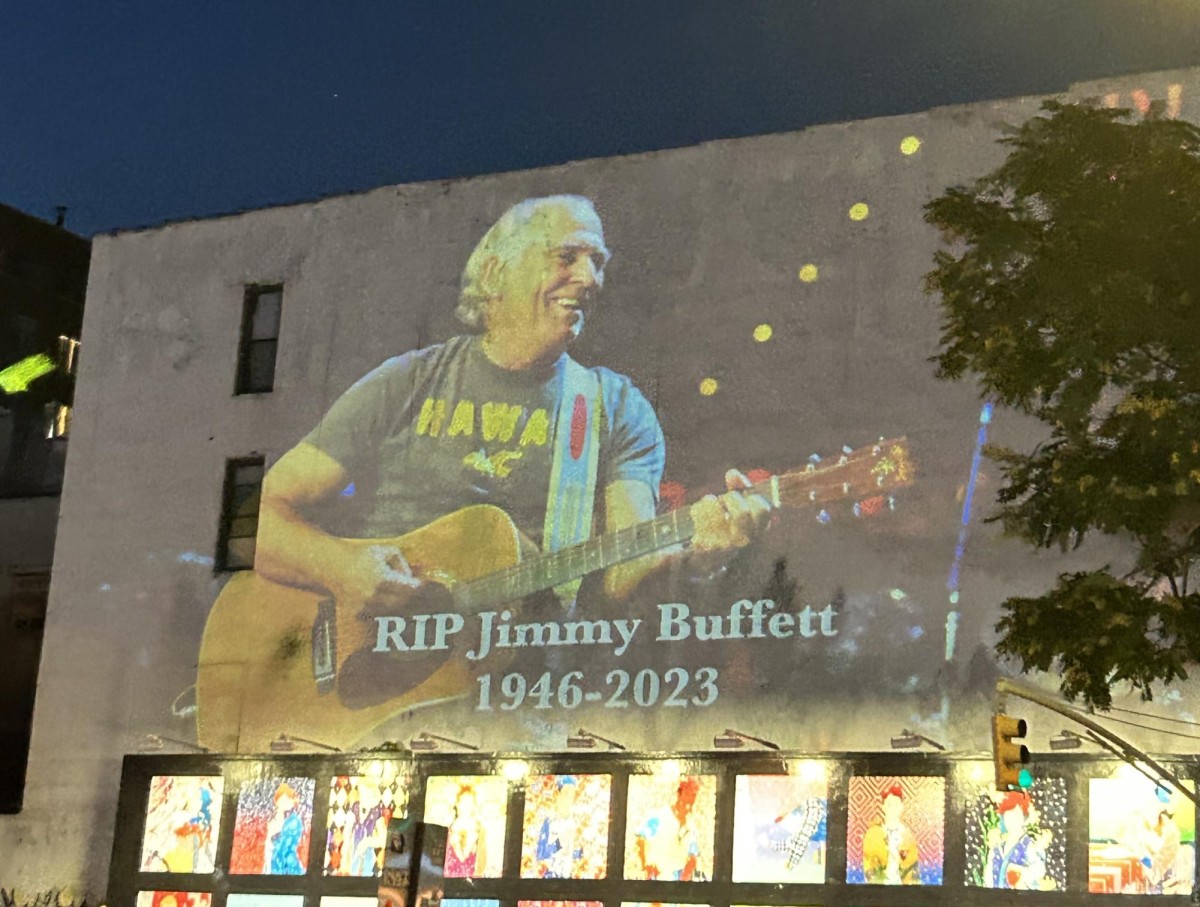 A man in a black shirt with a brown guitar is projected onto the side of a building.