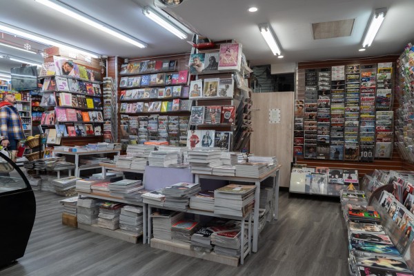The interior of a magazine shop, where hundreds of magazines are placed on the shelves on the walls and stacked on the table at the center of the space.