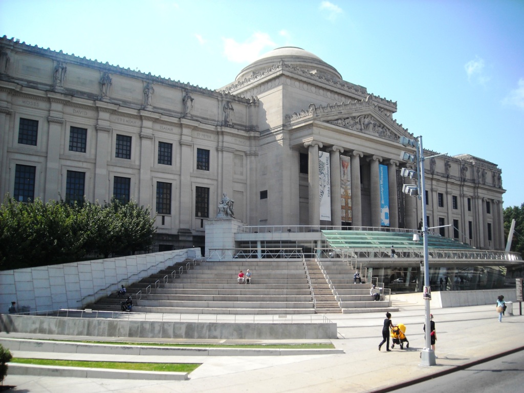 The exterior of the Brooklyn Museum which is a large white building with steps leading up the entrance.