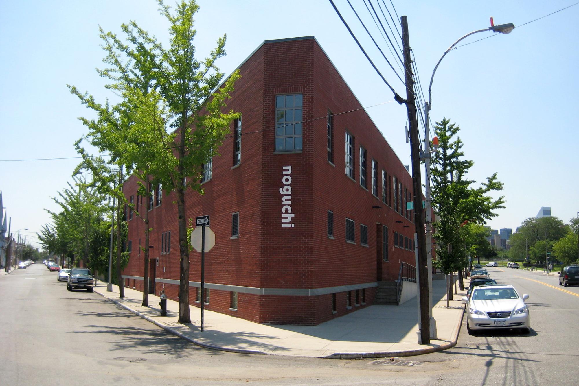 The exterior of The Noguchi Museum which is a red brick building with the word “noguchi” in white letters along the side.