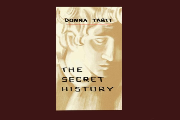 An illustration of a book cover which reads “THE SECRET HISTORY” and “DONNA TARTT” over an illustration of a male sculpture’s face. The cover is placed over a brown background.