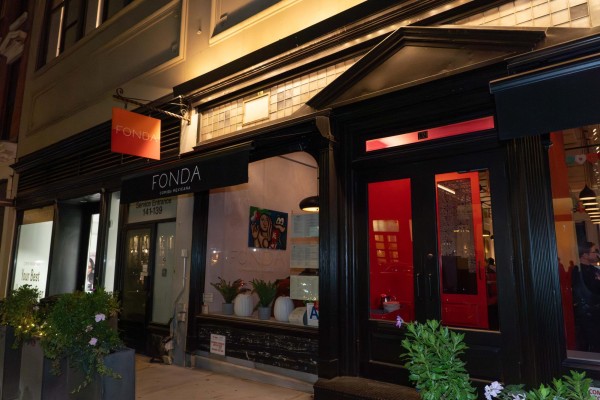 A storefront with a black door and red walls is inside the restaurant at the entrance. A red sign that says “FONDA” is hung above the entrance.