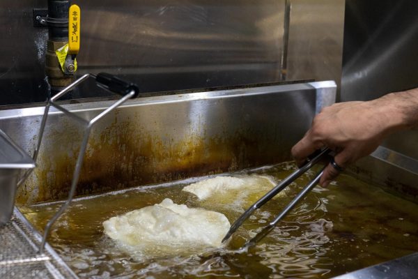 A restaurant worker uses a tong to fry two parathas in oil.