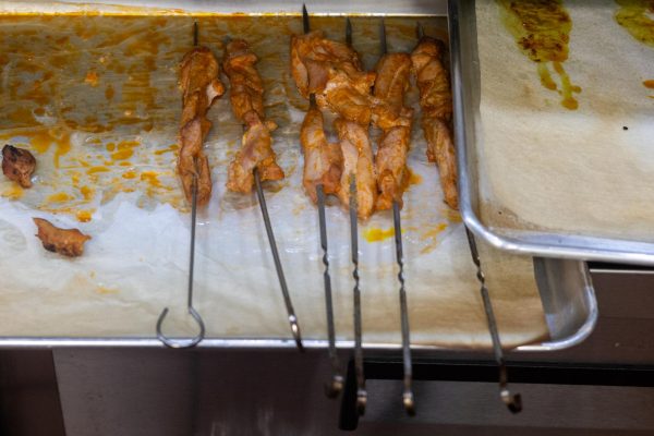 Six flame-grilled and marinated chicken skewers on a pan.