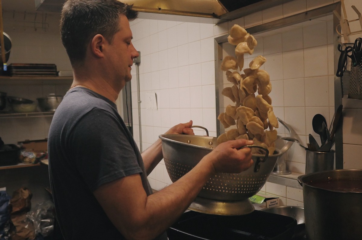 Dmytro Kovalenko is throwing a pierogi up in the air to evenly cover them in oil after boiling.