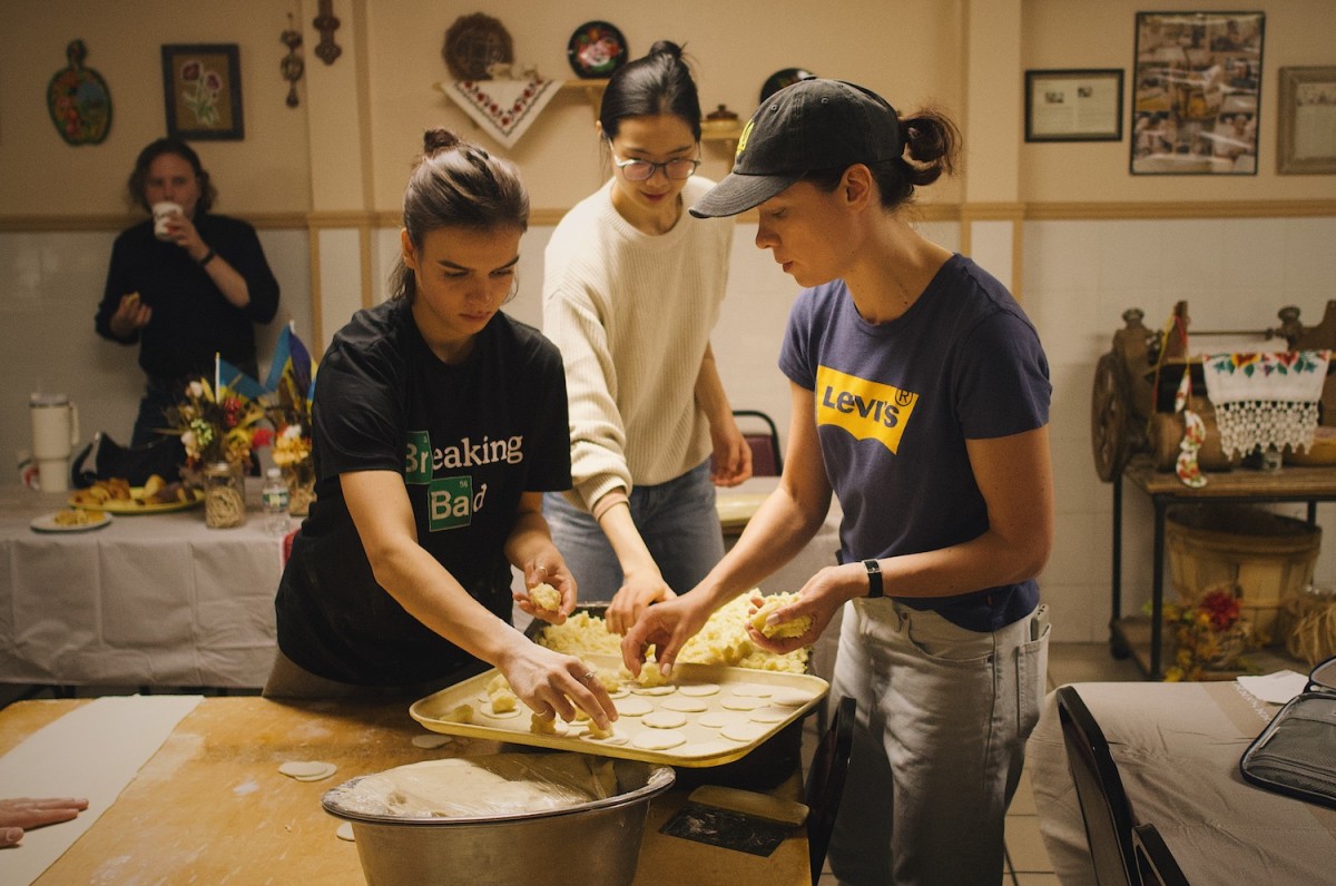 Three people are holding a tray and working on making small pastries.