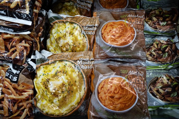 Bags of frozen potatoes and frozen sweet potatoes placed on a shelf among other frozen food products.