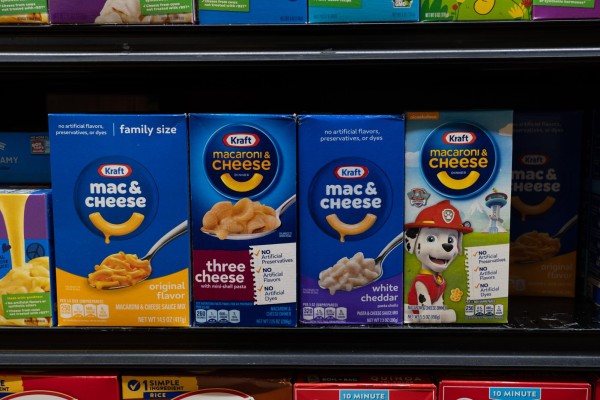 Many boxes of Kraft Mac & Cheese placed side by side on a supermarket shelf among other products.