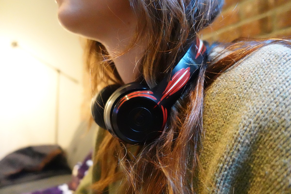 A girl has black headphones around her neck. The headphones have red and white vinyl paint designs on them.