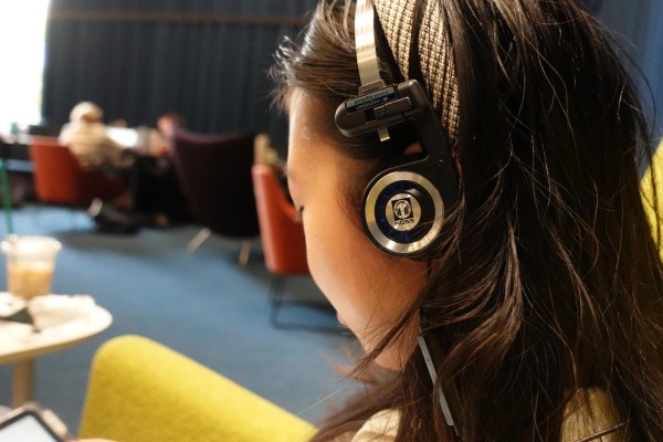 A girl wearing a black pair of headphones with the word “KOSS” under a logo of over-the-ear headphones placed in the center of the earmuff.