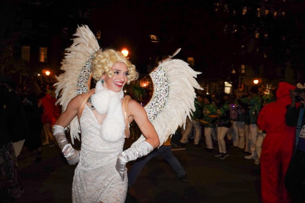 A person with white wings, a white dress and a white scarf dancing. They also have a short curly blond wing.