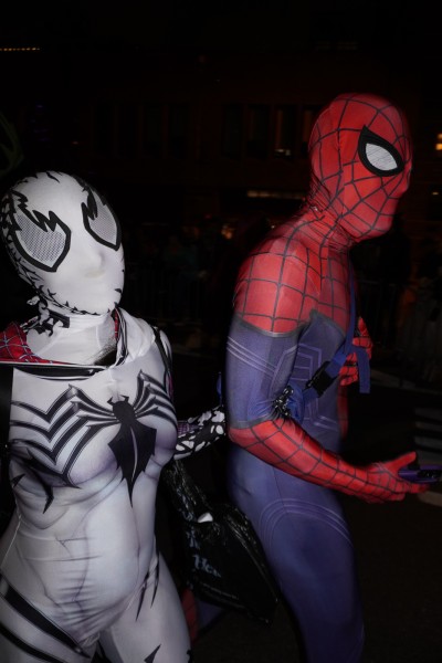 Two people dressed up in Spider-Man costumes standing side by side. The person on the right holds the arm of the person on the left with their left hand.