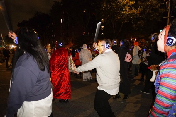 A crowd of people in costumes marching down a street wearing headphones.