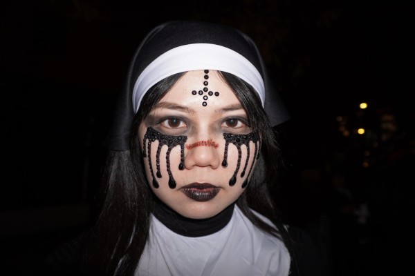 A girl dressed as a nun with a jewel upside down cross, black tears and fake stitches on her nose.