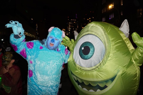 A man dressed in a blue monster costume with purple spots, as Sulley from Monsters, Inc., and another person dressed in a green monster costume with one big eye, as Mike from Monsters, Inc..