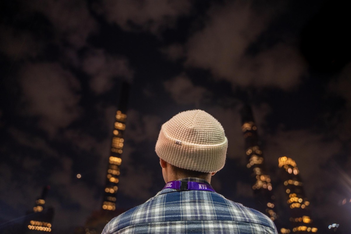 The back of a person in a white beanie, blue and white plaid shirt and purple N.Y.U. lanyard.