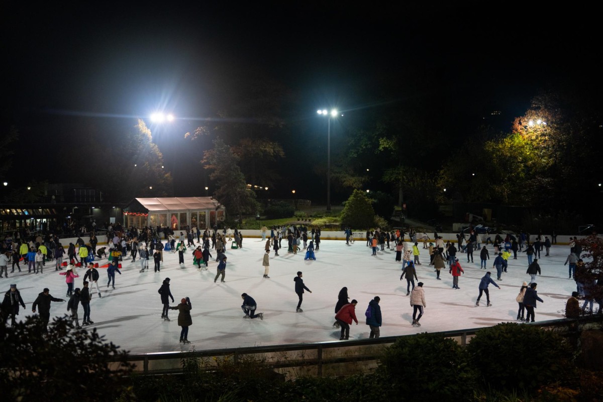 People in various colored winter outfits skate on the white ice rink.